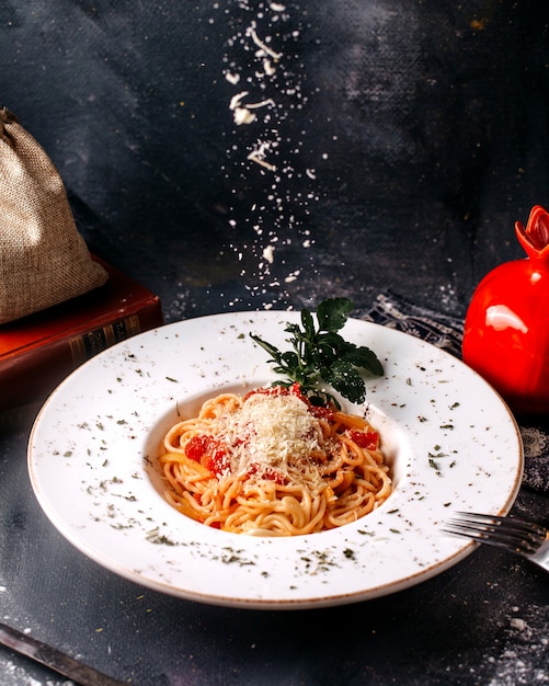 Piccante saporito saporito della pasta di vista frontale con i pomodori rossi e la foglia verde sul pavimento luminoso