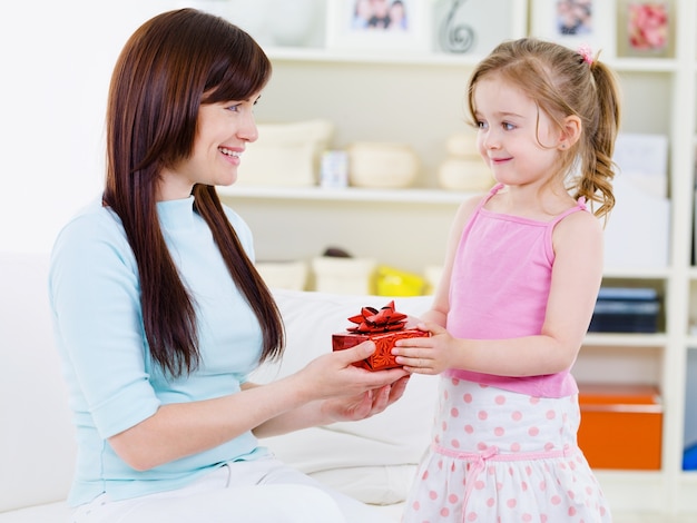 Piccola bella ragazza graziosa che dà un regalo a sua madre felice