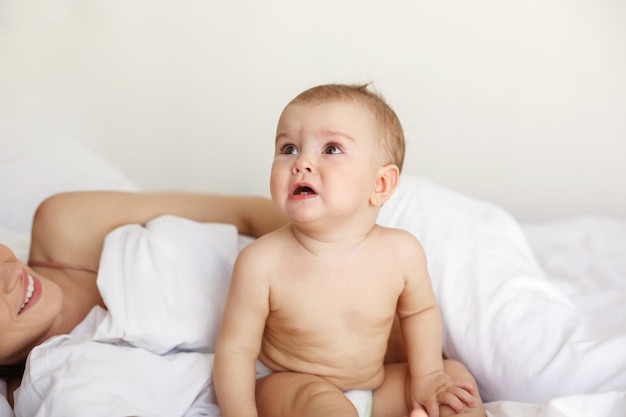 Piccola donna piacevole sveglia del bambino che grida menzogne con sua mamma sul letto a casa.