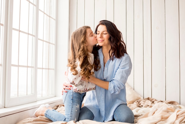 Piccola figlia che bacia madre sulla guancia sul letto