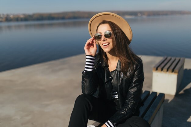 Piccola giovane donna modello ragazza seduta su una panchina in una giornata autunnale in riva al lago vestita in abiti casual