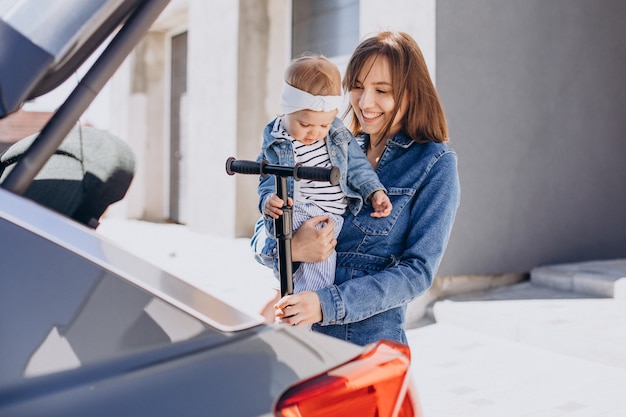 Piccola neonata che guida sul motorino con la sua mamma vicino alla macchina