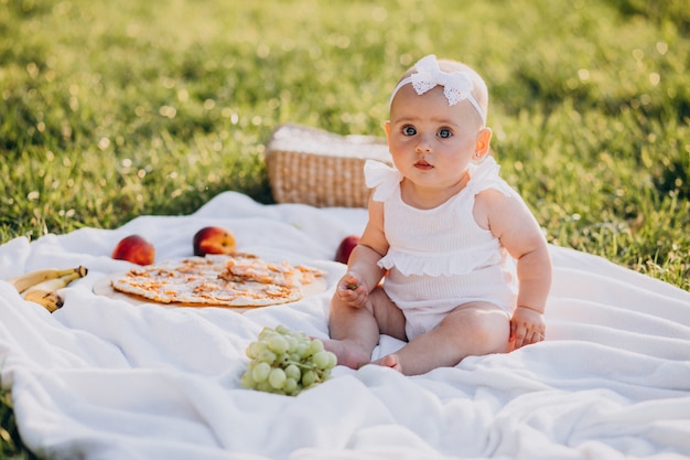 Piccola neonata sveglia che si siede sulla coperta nel parco