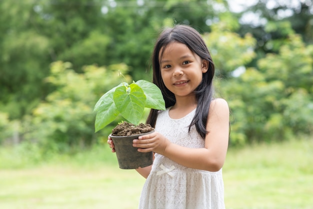 Piccola ragazza asiatica che tiene una pianta al parco