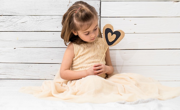 piccola ragazza carina in abito seduto su fondo di legno bianco con un cuore nelle sue mani, concetto di vacanza