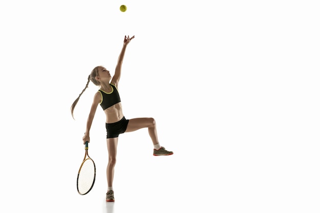 Piccola ragazza caucasica giocando a tennis isolato sul muro bianco