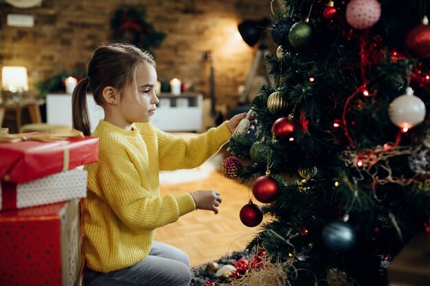 Piccola ragazza che decora l'albero di Natale nel soggiorno