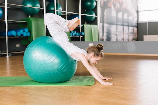 Piccola ragazza che fa gli esercizi con l'esercizio della palla nella palestra di forma fisica