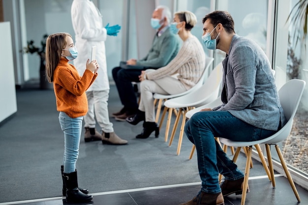 Piccola ragazza che scatta foto di suo padre con il touchpad nella sala d'attesa dell'ospedale