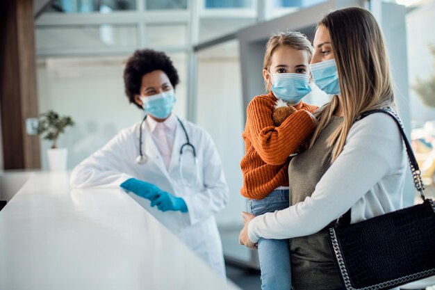 Piccola ragazza con la madre alla reception in ospedale durante la pandemia di coronavirus