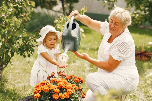 Piccola ragazza con la nonna senior giardinaggio nel giardino sul retro. Bambino in un cappello bianco.