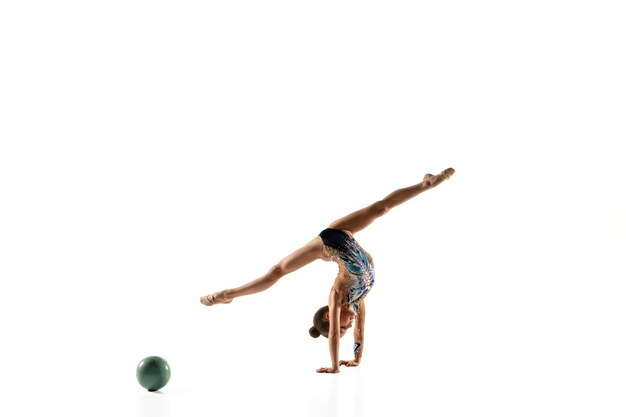 Piccola ragazza flessibile isolata sulla parete bianca. Piccola modella femminile come artista di ginnastica ritmica in calzamaglia luminosa. Grazia in movimento, azione e sport. Fare esercizi con la palla.