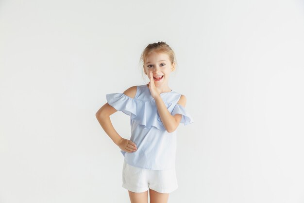 Piccola ragazza sorridente che posa in abbigliamento casual su studio bianco