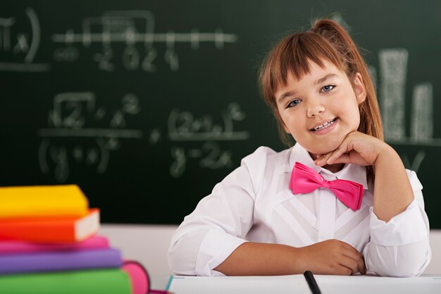 Piccola scolara sveglia che si siede in aula con i suoi libri