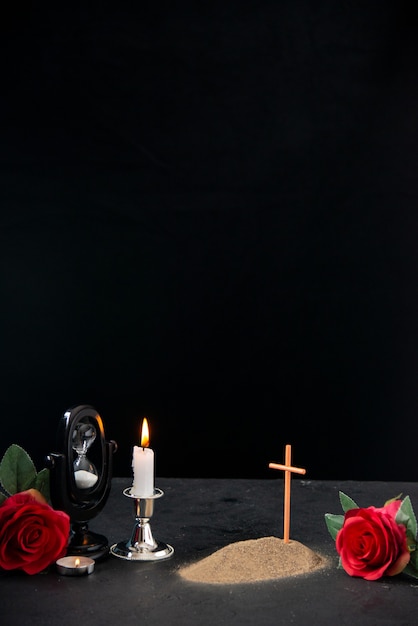 Piccola tomba con fiore rosso e candela accesa come memoria sulla superficie scura