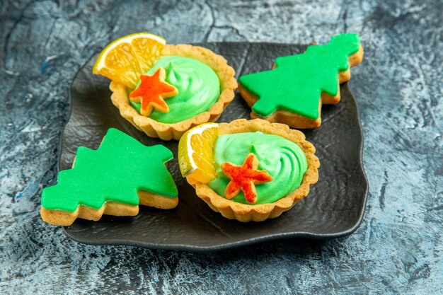 Piccole crostate vista dal basso con crema pasticcera verde biscotti per alberi di natale su banda nera su superficie grigia