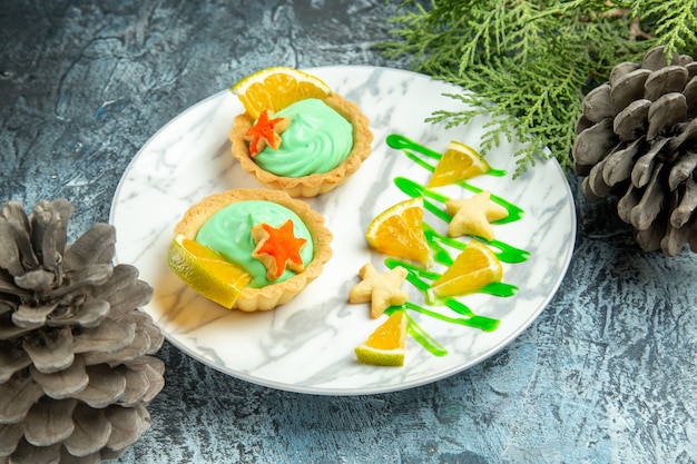 Piccole crostate vista dal basso con crema pasticcera verde e fetta di limone su pigne di ramo di pino piatto su superficie scura