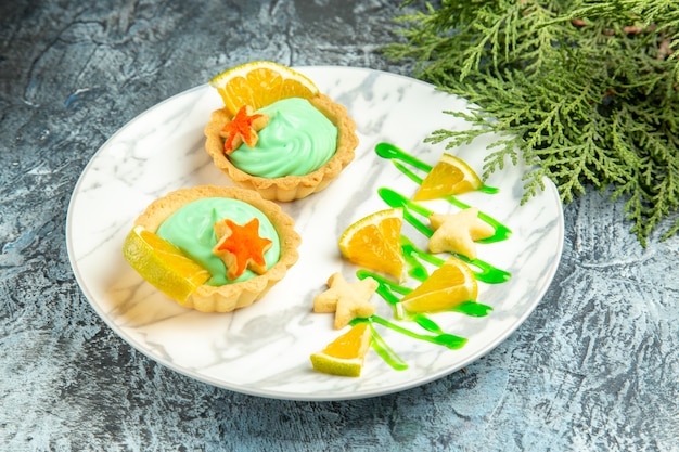 Piccole crostate vista dal basso con crema pasticcera verde e fetta di limone su ramo di pino piatto su superficie scura