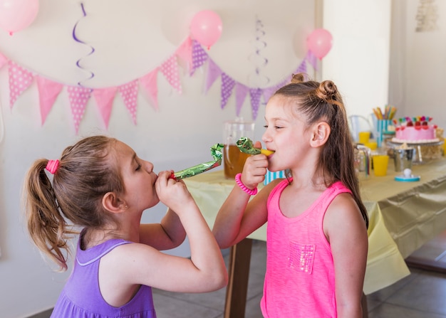 Piccole ragazze graziose che soffiano il corno del partito che gode nella festa