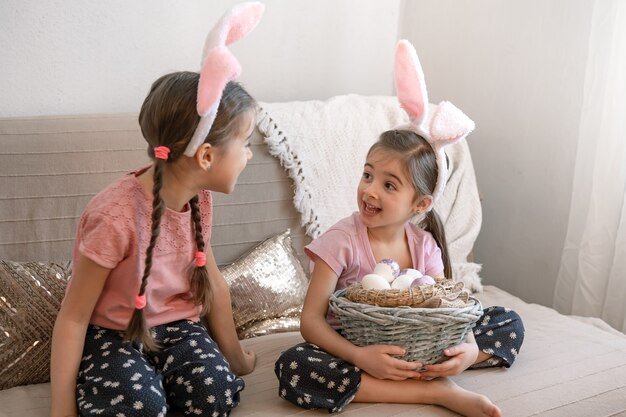 Piccole sorelle con orecchie da coniglio, con le uova di Pasqua a casa sul divano