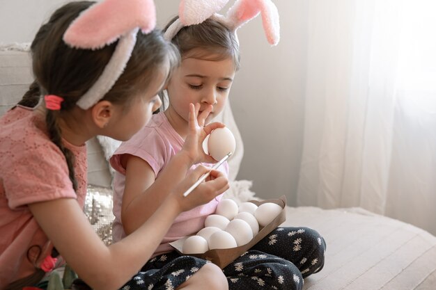 Piccole sorelle in orecchie da coniglio dipingono le uova di Pasqua sul divano di casa