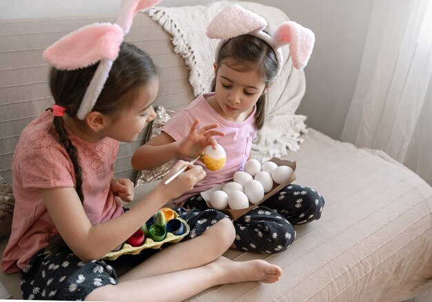 Piccole sorelle in orecchie da coniglio dipingono le uova di Pasqua sul divano di casa