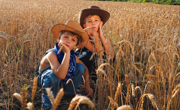 Piccoli cowboy adorabili che si siedono in un campo di grano durante il giorno