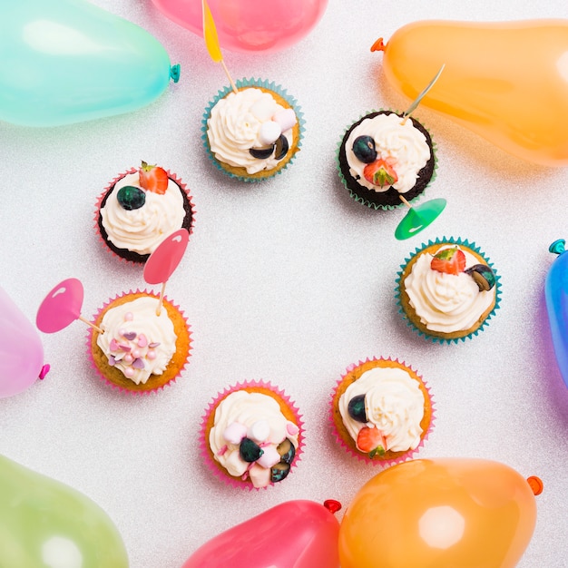 Piccoli dolci cupcakes con palloni ad aria sul tavolo luminoso