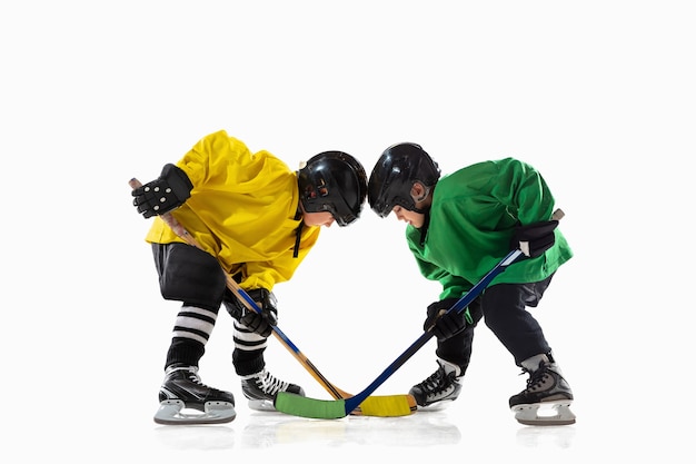 Piccoli giocatori di hockey con i bastoni sul campo da ghiaccio e la parete bianca dello studio