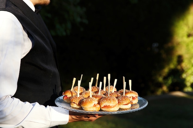 Piccoli hamburger serviti su un piatto tenuto dal cameriere