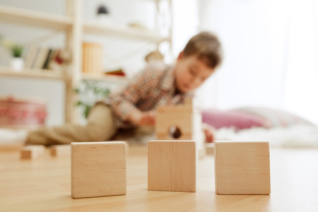 Piccolo bambino seduto sul pavimento bel ragazzo che palying con cubi di legno a casa