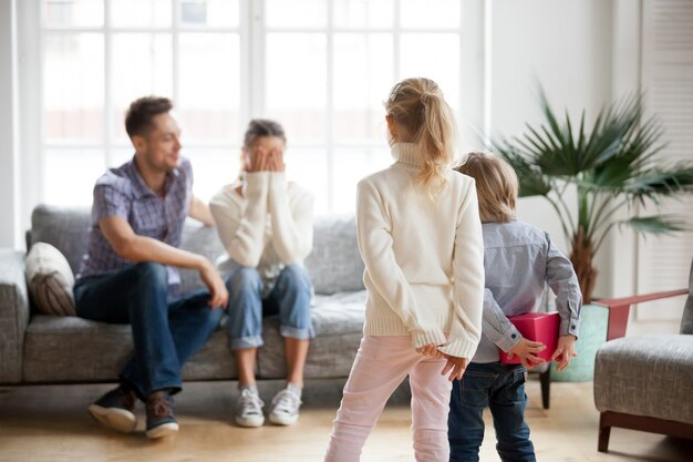 Piccolo figlio e figlia nascondendo presente preparazione a congratularsi con la madre