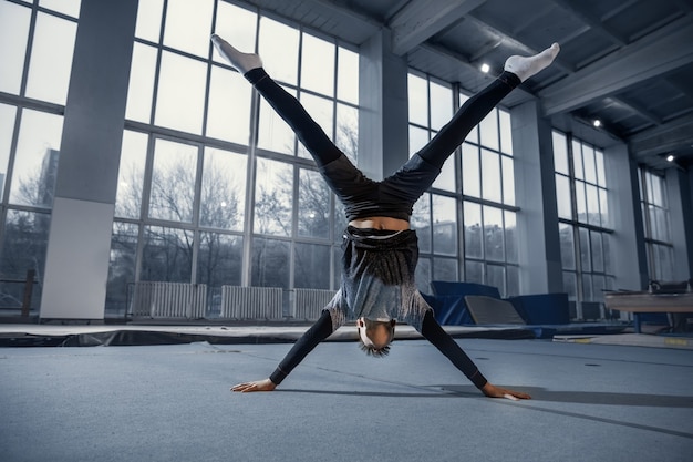 Piccolo ginnasta maschio allenamento in palestra, flessibile e attivo. Ragazzino in forma caucasica, atleta in abiti sportivi che praticano esercizi per la forza, l'equilibrio. Movimento, azione, movimento, concetto dinamico.