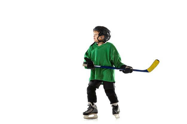 Piccolo giocatore di hockey con il bastone sul campo da ghiaccio, sfondo bianco studio. Sportsboy che indossa attrezzatura e casco, pratica, formazione. Concetto di sport, stile di vita sano, movimento, movimento, azione.