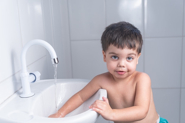 Piccolo neonato sveglio che lava la mano nel lavandino del bagno