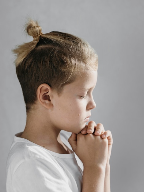 Piccolo ragazzo biondo di lato che prega
