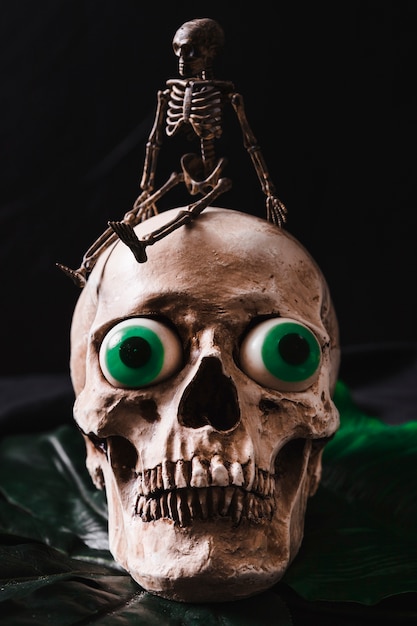 Piccolo scheletro che si siede sul cranio che si trova sulla foglia