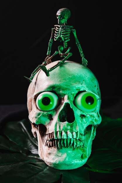 Piccolo scheletro seduto sul cranio illuminato