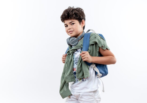 Piccolo scolaro soddisfatto che indossa la borsa posteriore e le cuffie isolate su fondo bianco