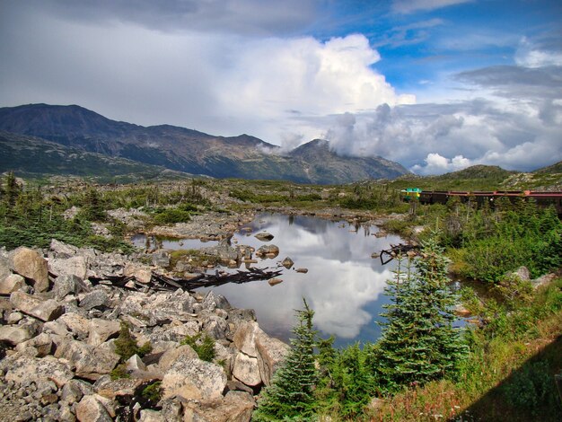 Piccolo stagno circondato da montagne e vegetazione sotto un cielo nuvoloso blu - perfetto per gli sfondi