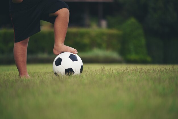 Piedi del ragazzino che tengono calcio al campo di erba