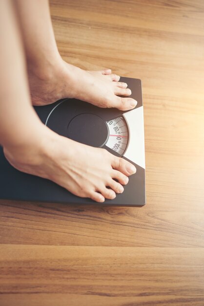 Piedi della donna che stanno sulla bilancia su fondo di legno