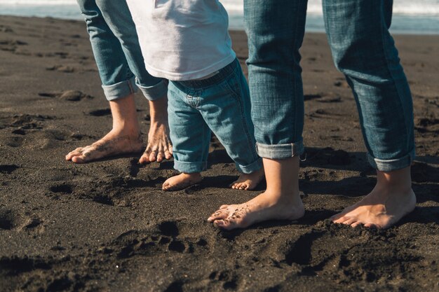 Piedi di bambino e genitori che camminano sulla costa sabbiosa