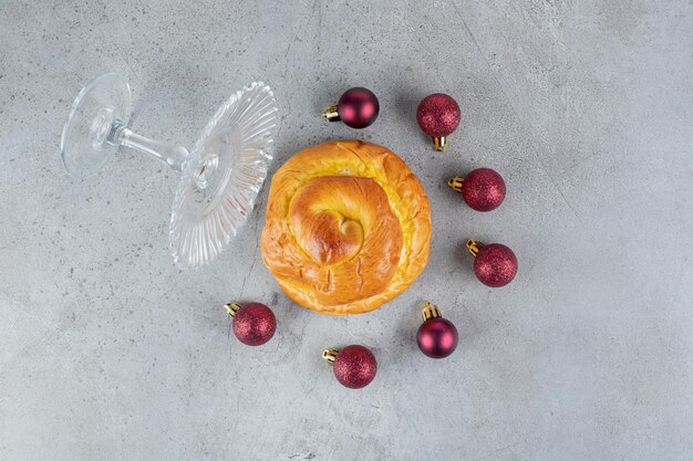 Piedistallo in vetro caduto, semicerchio con decorazioni per l'albero di Natale e panino dolce su superficie in marmo