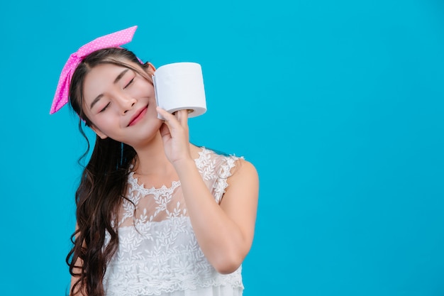 Pigiama bianco da portare della ragazza che tiene una carta del rotolo nella mano sull'azzurro.