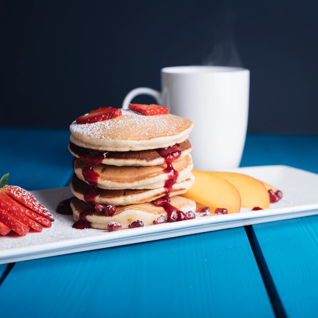 Pila casalinga dolce di pancake con sciroppo per la prima colazione sullo scrittorio blu