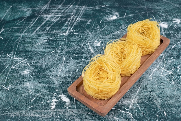 Pila di nidi di spaghetti crudi su tavola di legno. Foto di alta qualità