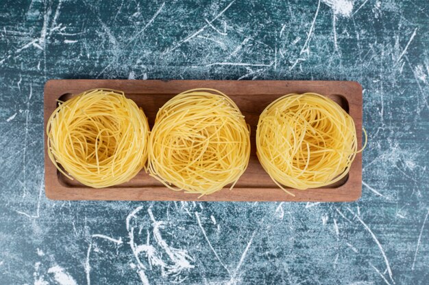 Pila di nidi di spaghetti crudi su tavola di legno. Foto di alta qualità