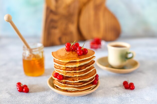 Pila di pancake fatti in casa con sciroppo di miele e frutti di bosco