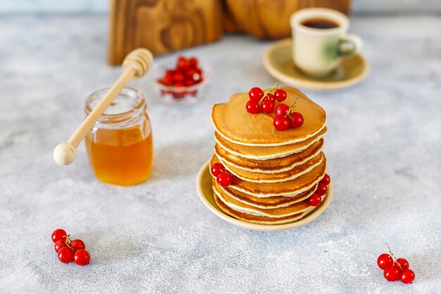 Pila di pancake fatti in casa con sciroppo di miele e frutti di bosco.